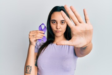 Fototapeta premium Young hispanic woman holding purple ribbon awareness with open hand doing stop sign with serious and confident expression, defense gesture