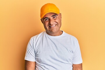Mature middle east man with mustache wearing casual white tshirt and yellow cap with a happy and cool smile on face. lucky person. - obrazy, fototapety, plakaty