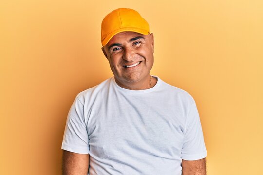 Mature middle east man with mustache wearing casual white tshirt and yellow cap with a happy and cool smile on face. lucky person.