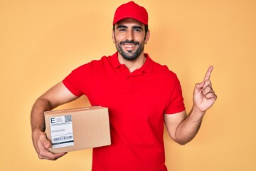 Handsome hispanic man with beard holding delivery package smiling happy pointing with hand and finger to the side