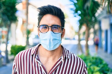 Young handsome hispanic man with beard outdoors wearing coronavirus safety mask