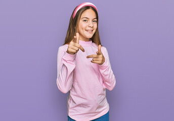 Beautiful brunette little girl wearing casual turtleneck sweater pointing fingers to camera with happy and funny face. good energy and vibes.