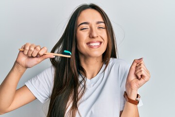 Young hispanic girl holding toothbrush with toothpaste screaming proud, celebrating victory and success very excited with raised arm