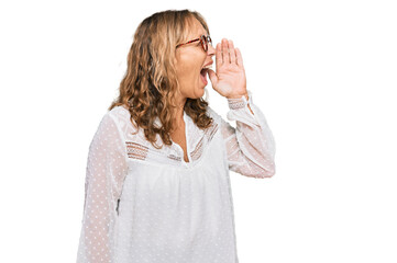 Middle age blonde woman wearing casual white shirt and glasses shouting and screaming loud to side with hand on mouth. communication concept.