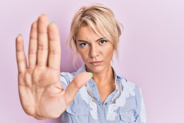 Young blonde girl wearing casual clothes doing stop sing with palm of the hand. warning expression with negative and serious gesture on the face.