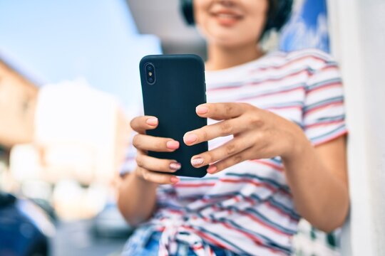 Young latin girl smiling happy using smartphone and headphones at the city