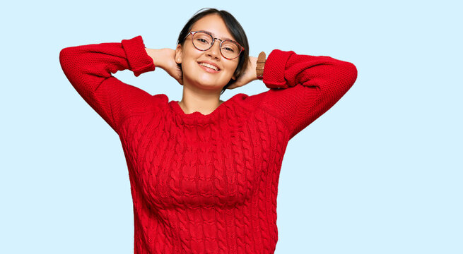 Young beautiful hispanic woman with short hair wearing casual sweater and glasses relaxing and stretching, arms and hands behind head and neck smiling happy