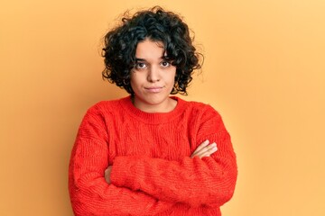 Young hispanic woman with curly hair wearing casual winter sweater skeptic and nervous, disapproving expression on face with crossed arms. negative person.