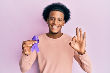 African american man with afro hair holding awareness purple ribbon doing ok sign with fingers,...