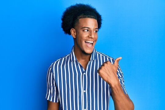 African american man with afro hair wearing casual clothes pointing thumb up to the side smiling happy with open mouth