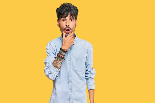 Young hispanic man wearing casual clothes looking fascinated with disbelief, surprise and amazed expression with hands on chin