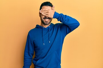 Young hispanic man wearing casual clothes smiling and laughing with hand on face covering eyes for surprise. blind concept.