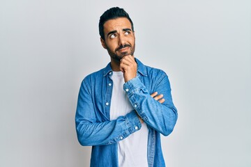 Young hispanic man wearing casual clothes thinking concentrated about doubt with finger on chin and...