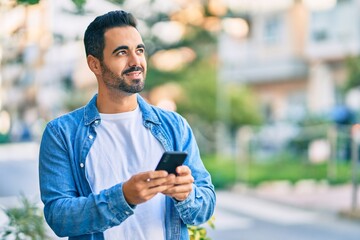 Young hispanic man smiling happy using smartphone at the city.