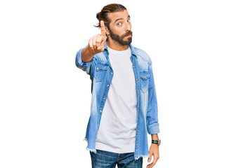 Attractive man with long hair and beard wearing casual denim jacket pointing with finger up and angry expression, showing no gesture