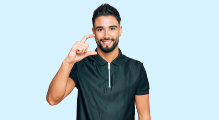 Naklejka premium Young man with beard wearing sportswear smiling and confident gesturing with hand doing small size sign with fingers looking and the camera. measure concept.