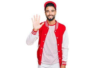 Young man with beard wearing baseball uniform showing and pointing up with fingers number five while smiling confident and happy.