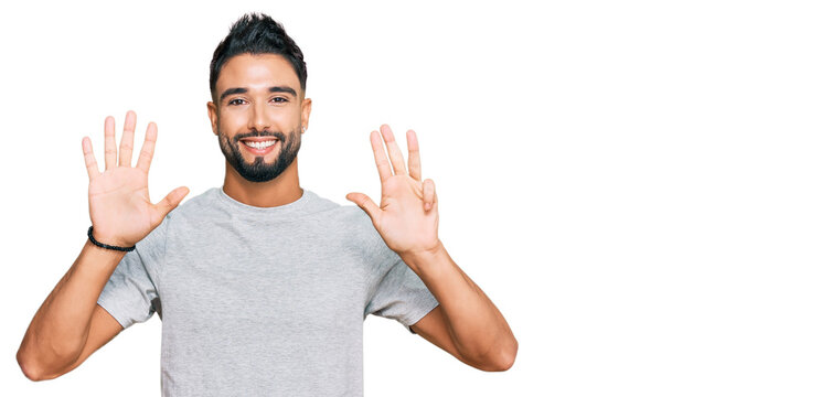 Young man with beard wearing casual grey tshirt showing and pointing up with fingers number nine while smiling confident and happy.