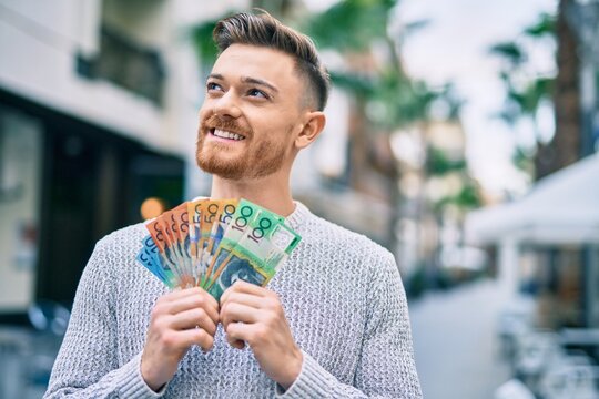 Young caucasian man smiling happy holding australian dollars at the city.