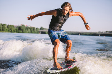 Active wakesurfer jumping on wake board down the river waves. Surfer on wave. Male athlete training on wakesurf training. Active water sports in open air on board. A man catches a wave on surf