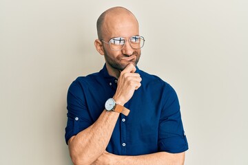 Young hispanic man wearing casual clothes and glasses serious face thinking about question with hand on chin, thoughtful about confusing idea