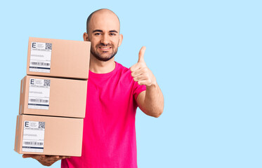 Young handsome man holding delivery package smiling happy and positive, thumb up doing excellent and approval sign