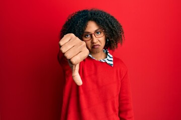 Beautiful african american woman with afro hair wearing sweater and glasses looking unhappy and angry showing rejection and negative with thumbs down gesture. bad expression.