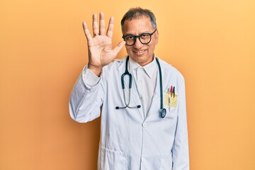 Middle age indian man wearing doctor coat and stethoscope showing and pointing up with fingers number five while smiling confident and happy.