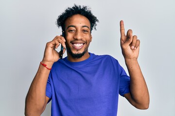 Fototapeta premium Young african american man with beard having conversation talking on the smartphone smiling with an idea or question pointing finger with happy face, number one