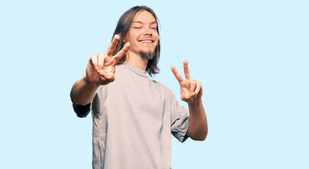 Handsome caucasian man with long hair wearing casual clothes smiling looking to the camera showing fingers doing victory sign. number two.