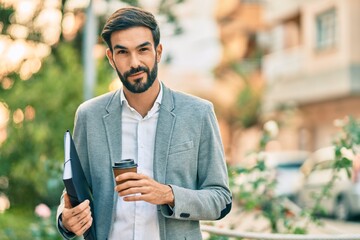 Young hispanic businessman smiling happy drinking take away coffee at the city.