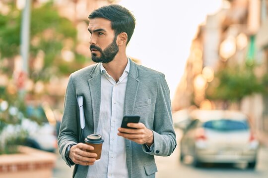 Young hispanic businessman with serious expression using smartphone and drinking coffee at the city.
