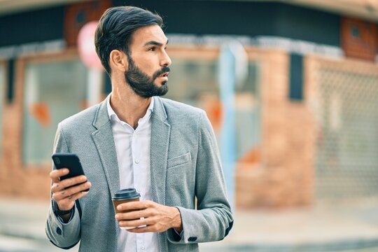 Young hispanic businessman with serious expression using smartphone and drinking coffee at the city.