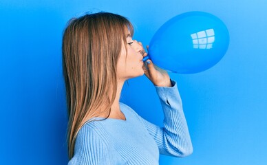 Caucasian woman blowing a balloon over blue background