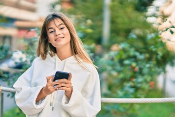 Caucasian sporty teenager girl smiling happy using smartphone at the city.