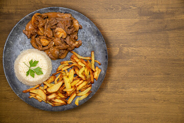 filet mignon stroganoff in an dark stone dish with white rice and french fries. Top view