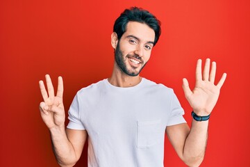 Naklejka premium Young hispanic man wearing casual white tshirt showing and pointing up with fingers number eight while smiling confident and happy.