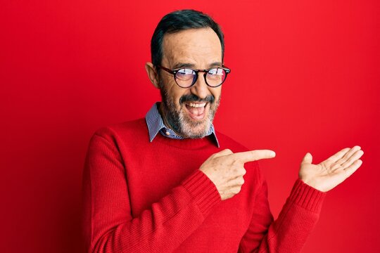 Middle age hispanic man wearing casual clothes and glasses amazed and smiling to the camera while presenting with hand and pointing with finger.