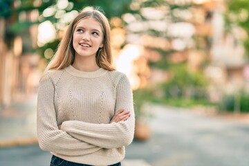 Beautiful caucasian teenager with arms crossed smiling happy standing at the city.