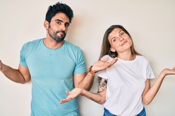 Beautiful young couple of boyfriend and girlfriend together clueless and confused expression with arms and hands raised. doubt concept.
