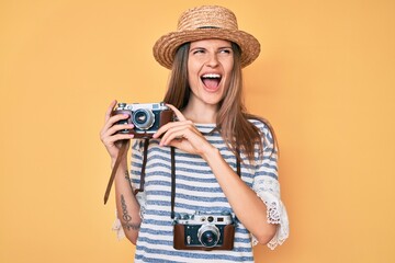 Beautiful caucasian tourist woman holding vintage camera angry and mad screaming frustrated and furious, shouting with anger. rage and aggressive concept.