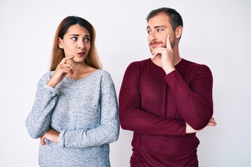 Beautiful couple wearing casual clothes serious face thinking about question with hand on chin,...