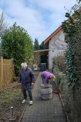 Senior woman and daughter cleaning a pathway. Seasonal spring garden work.