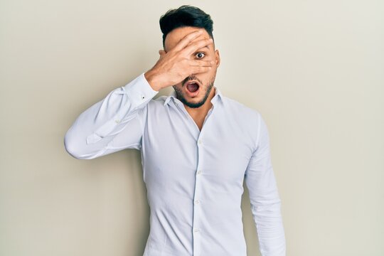 Young arab man wearing casual clothes peeking in shock covering face and eyes with hand, looking through fingers afraid