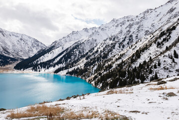 Fototapeta na wymiar Big Almaty Lake in Kazakhstan in a cold winter day. Plenty of snow visible around the Alpine Lake located in the Trans Ili Alatau mountains.