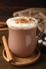 Glass cup of hot cocoa with whipped cream and aromatic cinnamon on wooden table