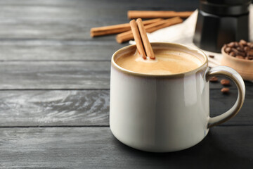 Cup of hot coffee with aromatic cinnamon on black wooden table. Space for text