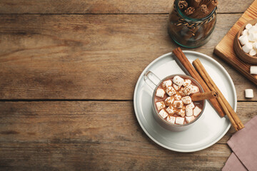 Glass cup of hot cocoa with aromatic cinnamon and marshmallows on wooden table, flat lay. Space for text