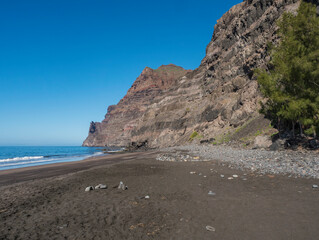View of empty sand beach Playa de Guigui with rocky cliffs in west part of the Gran Canaria island, accessible only on foot from Barranco de Guigui Grande gorge or by boat. Canary Islands, Spain