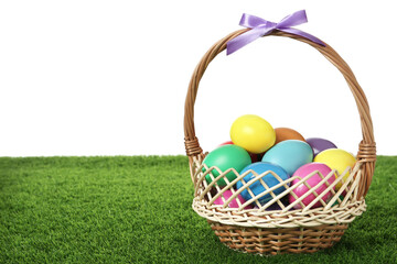 Wicker basket with bow and bright painted Easter eggs on green grass against white background. Space for text